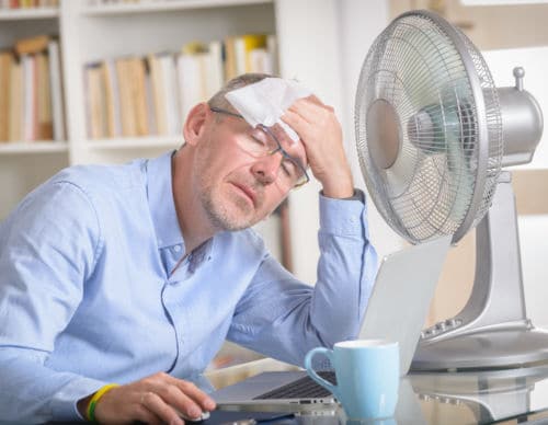 Man suffers from heat while working in the office and tries to cool off by the fan
